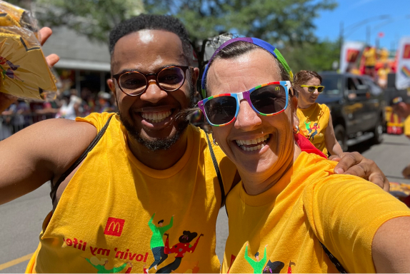 A selfie of two McDonald’s colleagues smiling with their arms around each other as they pause for a picture at a local Pride Parade